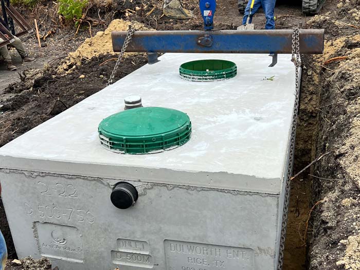 Crew lowering a septic tank into an excavated hole in Charlotte
