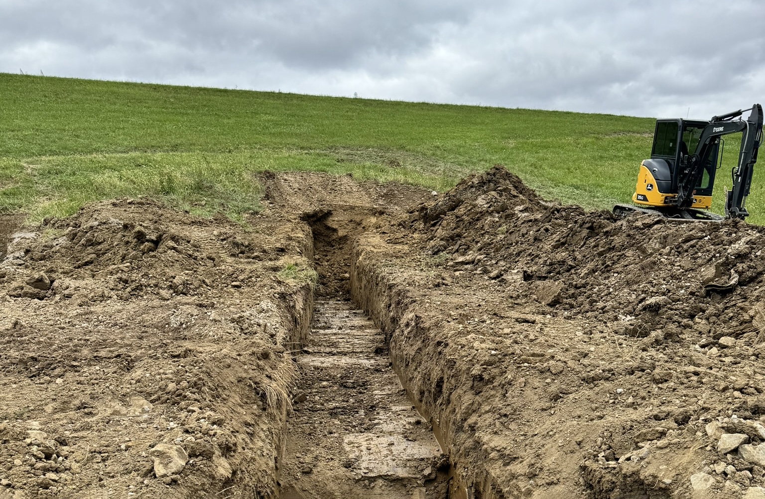Mini excavator trenching in an open field for utility or septic work